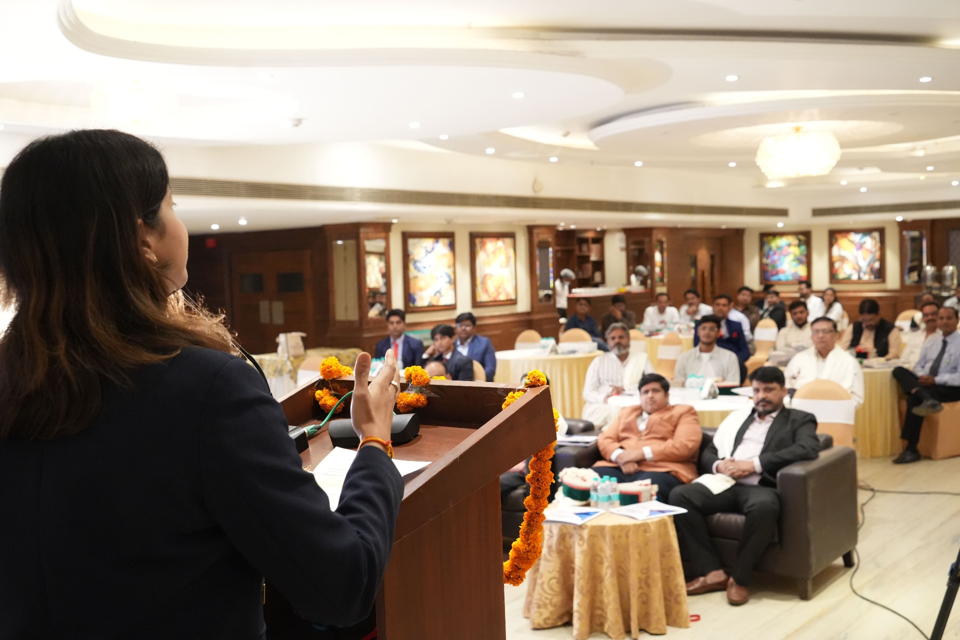 Arika speaker addressing distributors and partners from a marigold-decorated podium