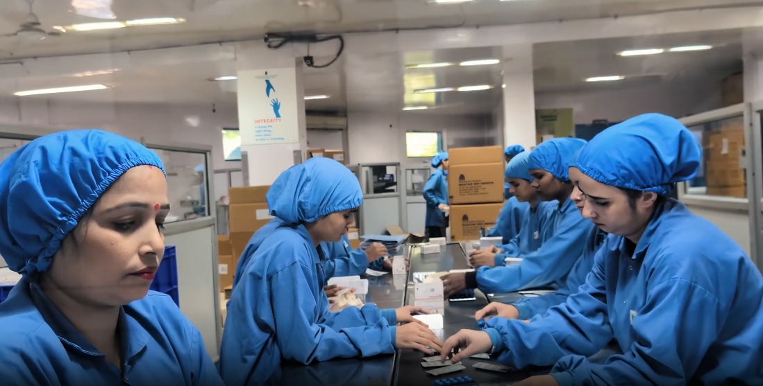 Packaging team in blue gowns inspecting blister strips on production line